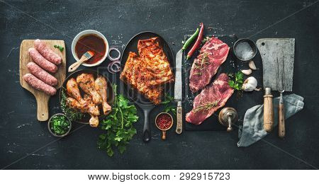 Various kinds of grill and bbq meats with vintage kitchen and butcher utensils. Chicken legs, steaks, sausages, pork ribs with herbs, spices, sauces and ingredients for grilling