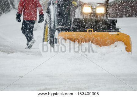 Winter storm conditions with snow removal on city streets with snow plow plowing the roads and pedestrian person walking through snow storm in icy winter weather background image