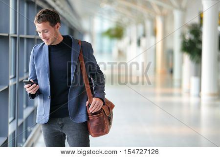 Business man using mobile phone app in airport. Young business professional man texting smartphone walking inside office building or airport terminal. Handsome man wearing stylish suit jacket indoors.