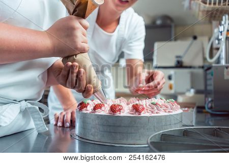 Confectioner or pastry chefs finishing cake with pastry bag, close-up on hands