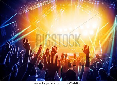 Photo of young people having fun at rock concert, active lifestyle, fans applauding to famous music band, nightlife, DJ on the stage in the club, crowd dancing on dance-floor, night performance