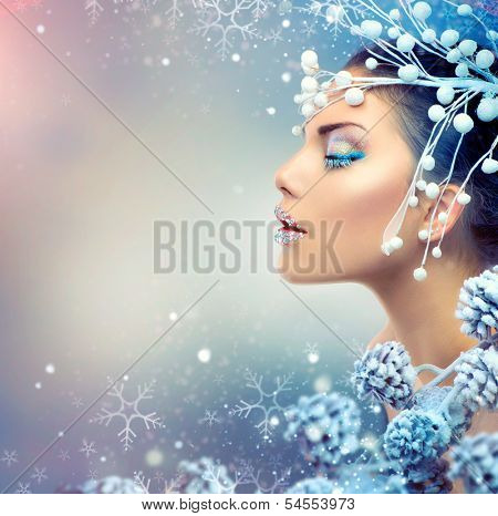 Winter Beauty Woman. Christmas Girl Makeup. Holiday Make-up. Snow Queen High Fashion Portrait over Blue Snow Background. Eyeshadows, False Eyelashes and Crystals on the Lips. Copy Space for Your Text 