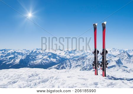 Pair of skis in snow with copy space. Red skis standing in snow with winter mountains in background. Winter holiday vacation and skiing concept. 