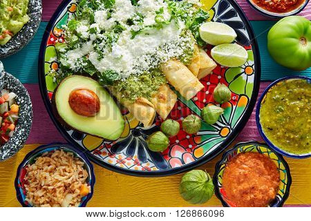 Green enchiladas Mexican food with guacamole and sauces on colorful table