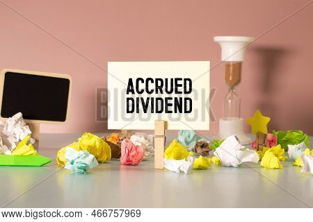 On The Business Card Is The Text Accrued Dividend On The Background Of Dollar Bills On The Table