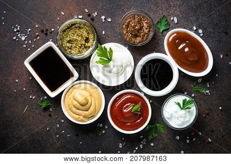 Set of sauces - ketchup, mayonnaise, mustard soy sauce, bbq sauce, pesto, mustard grains and pomegranate sauce on dark rusty stone or metal background. Top view.