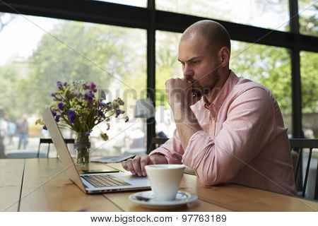 Thoughtful businessman work on notebook while sitting at wooden table in modern coffee shop interior