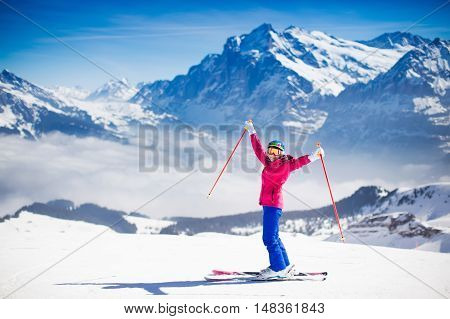 Young active woman skiing in mountains. Female skier kid with safety helmet goggles and poles enjoying sunny winter day in Swiss Alps. Ski race for adults. Winter and snow sport in alpine resort.