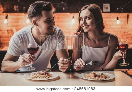 Smiling Young Couple Have Dinner And Drink Red Wine. Romantic Dinner In Modern Kitchen. Romantic Din