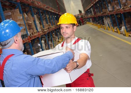 one worker in uniform receiving box from another  in warehouse