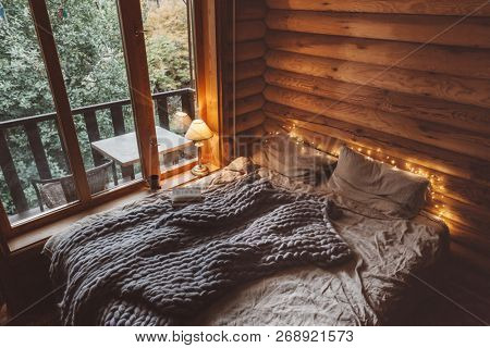 Rustic interior decoration of log cabin bedroom. Cozy warm blanket on bed by window.