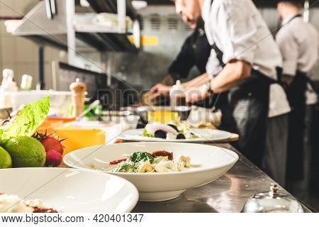 Professional Chef Cooking In The Kitchen Restaurant At The Hotel, Preparing Dinner. A Cook In An Apr