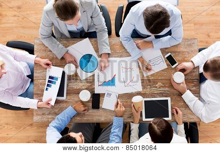 business, people, statistics and team work concept - close up of creative team with charts and gadgets meeting and drinking coffee in office