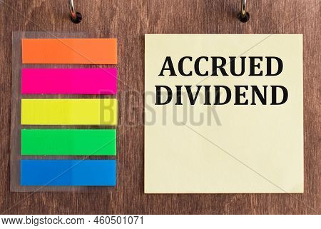 On The Business Card The Text Is Accrued Dividend On A Wooden Background Next To Colored Sticky Note