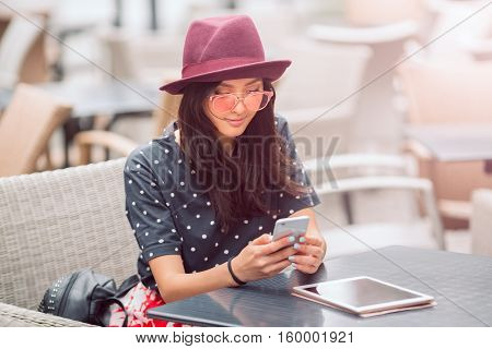 Cafe city lifestyle woman on phone texting text message on smartphone app sitting outdoor in trendy urban cafe. Cool young modern mixed race Asian Caucasian female model in fashion retro look style