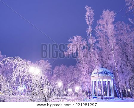 Amazing winter landscape in evening park. Gazebo, lantern lights, snow and frosty trees. Artistic picture. Beauty world.