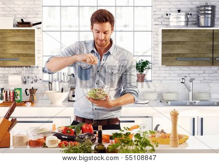 Handsome man cooking at home preparing salad in kitchen.