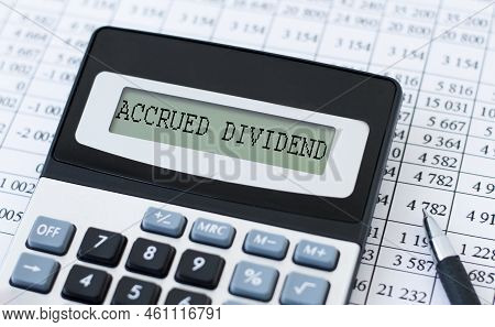 Business Concept. Accrued Dividend Inscription On The Calculator Screen On The Background Of Reports