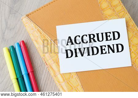 On The Business Card The Text Is Accrued Dividend Lies On A Yellow Notebook On A Wooden Table