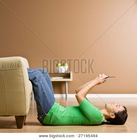 Woman laying on floor in livingroom text messaging on cell phone