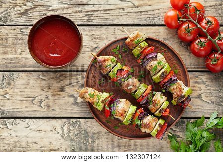 Barbecued turkey or chicken meat shish kebab skewers with ketchup sauce, chopped parsley and tomatoes on rustic wooden table background. Traditional barbecue grill food