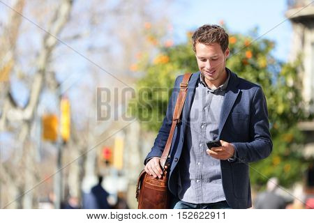 Young urban businessman professional on smartphone walking in street using mobile phone app texting sms message on smartphone wearing smart casual jacket. City lifestyle commute person walking.