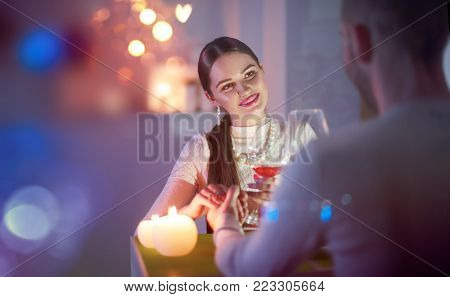 Romantic dinner. Young couple Toasting Wine Glass In restaurant or at home, holding hands, love Dating. Beautiful brunette woman on romantic dinner drinking at bar. Date. Valentines Day celebrating. 