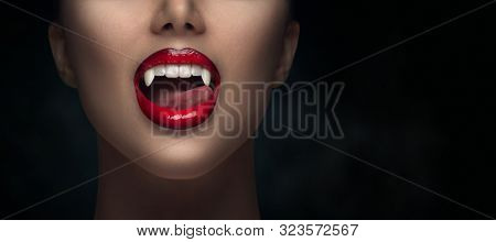 Sexy Vampire Woman's red bloody lips close-up. Vampire girl licking fangs with tongue. Fashion Glamour Halloween art design. Close up of female vampire mouth, teeth. Isolated on black background