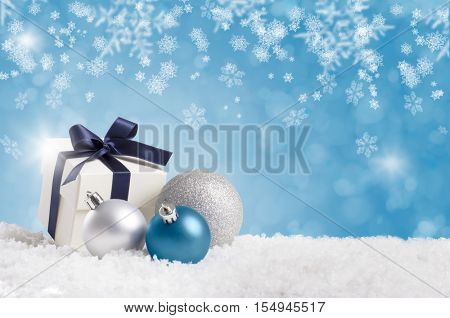 Christmas gift wrapped with blue ribbon with silver balls on white snow. Little christmas present on snow with copy space on blue background. Blue and silver xmas decoration with copyspace.