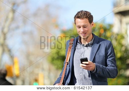 Young urban businessman professional on smartphone walking in street using app texting sms message on smartphone wearing jacket on Passeig de Gracia, Barcelona, Catalonia, Spain.