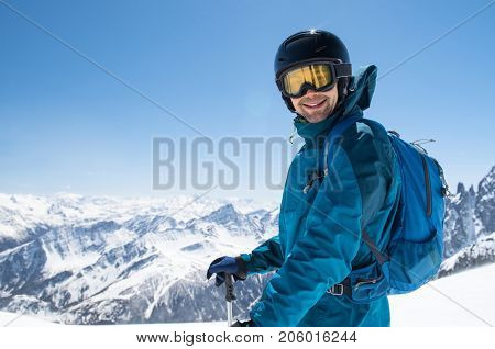 Cheerful skier looking at camera before starting to skiing. Happy man enjoying holiday in winter season. Smiling mountaineer skier in winterwear with ski equipment and copy space.