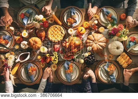 Group of friends or family members giving thanks to God at festive turkey dinner table together. Thanksgiving celebration traditional dinner concept