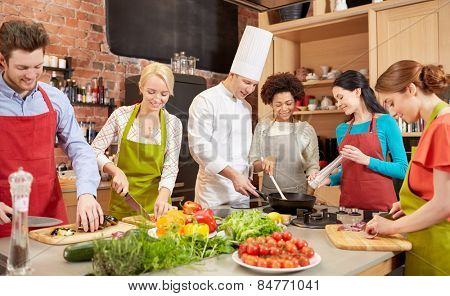 cooking class, culinary, food and people concept - happy group of friends and male chef cook cooking in kitchen