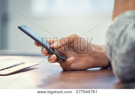 Closeup hand of woman using smartphone on wooden table. Businesswoman typing text message on smart phone. Casual lady hand holding mobile phone with blank screen at office.