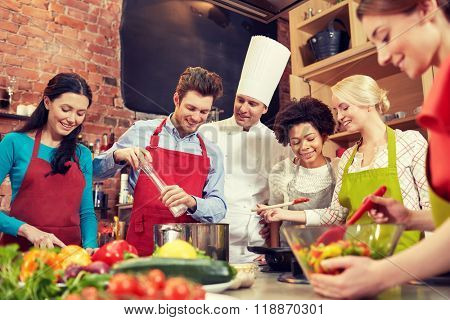 cooking class, culinary, food and people concept - happy group of friends and male chef cook cooking in kitchen