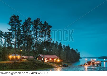 Sweden. Beautiful Red Swedish Wooden Log Cabin House On Rocky Island Coast In Summer Night Evening. 