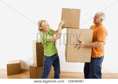 Middle-aged man holding cardboard moving boxes while woman places one on stack.