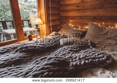 Rustic interior decoration of log cabin bedroom. Cozy warm blanket on bed by window.