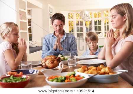 Family Saying Prayer Before Eating Roast Dinner