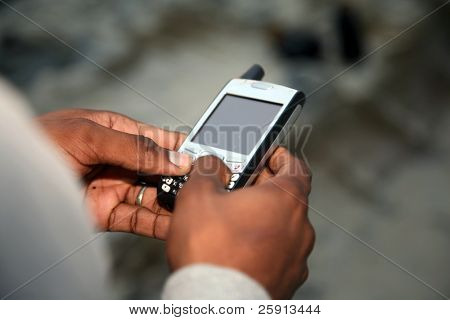 a african american man text messages outside on the beach