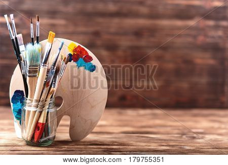 Set of different brushes and acrylic paints to paint scattered on a dark wooden table.Artist workplace background.Art tools.Creativity, visual art concept.Paints brushes and paints palette. Copy space