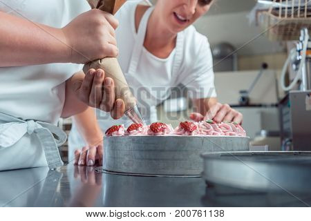 Confectioner or pastry chefs finishing cake with pastry bag, close-up on hands