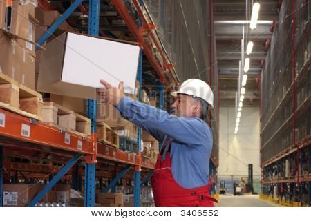 Worker In Uniform Putting Box On Shelves In Warehouse