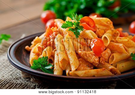 Penne pasta in tomato sauce with chicken, tomatoes decorated with parsley on a wooden table