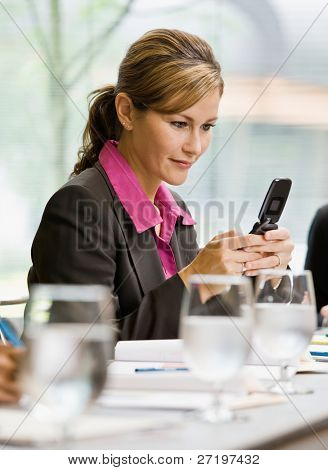 Businesswoman text messaging on cell phone in conference room