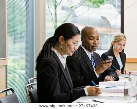 Businessman with co-workers text messaging on cell phone in conference room