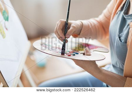 art, creativity and people concept - close up of artist with palette and brush painting still life on paper at studio