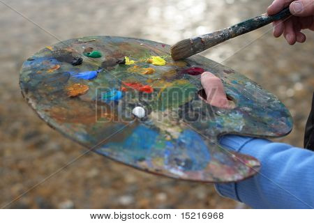 Mature artist with palette and brush painting a coastal landscape focus on brush.