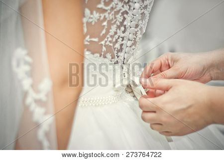 Wedding. Mother Preparing Bride For The Wedding Day. Bridesmaid Helps Fasten A Wedding Dress The Bri