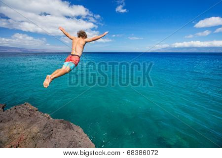 Man jumping off cliff into the ocean. Summer fun lifestyle.